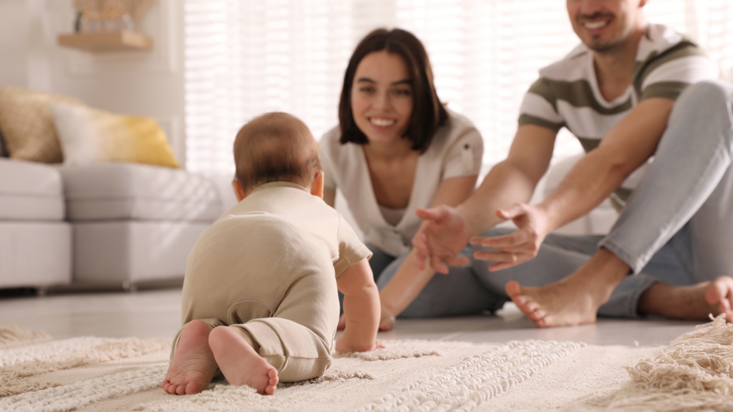 Happy parents watching their cute baby crawl on floor at home
