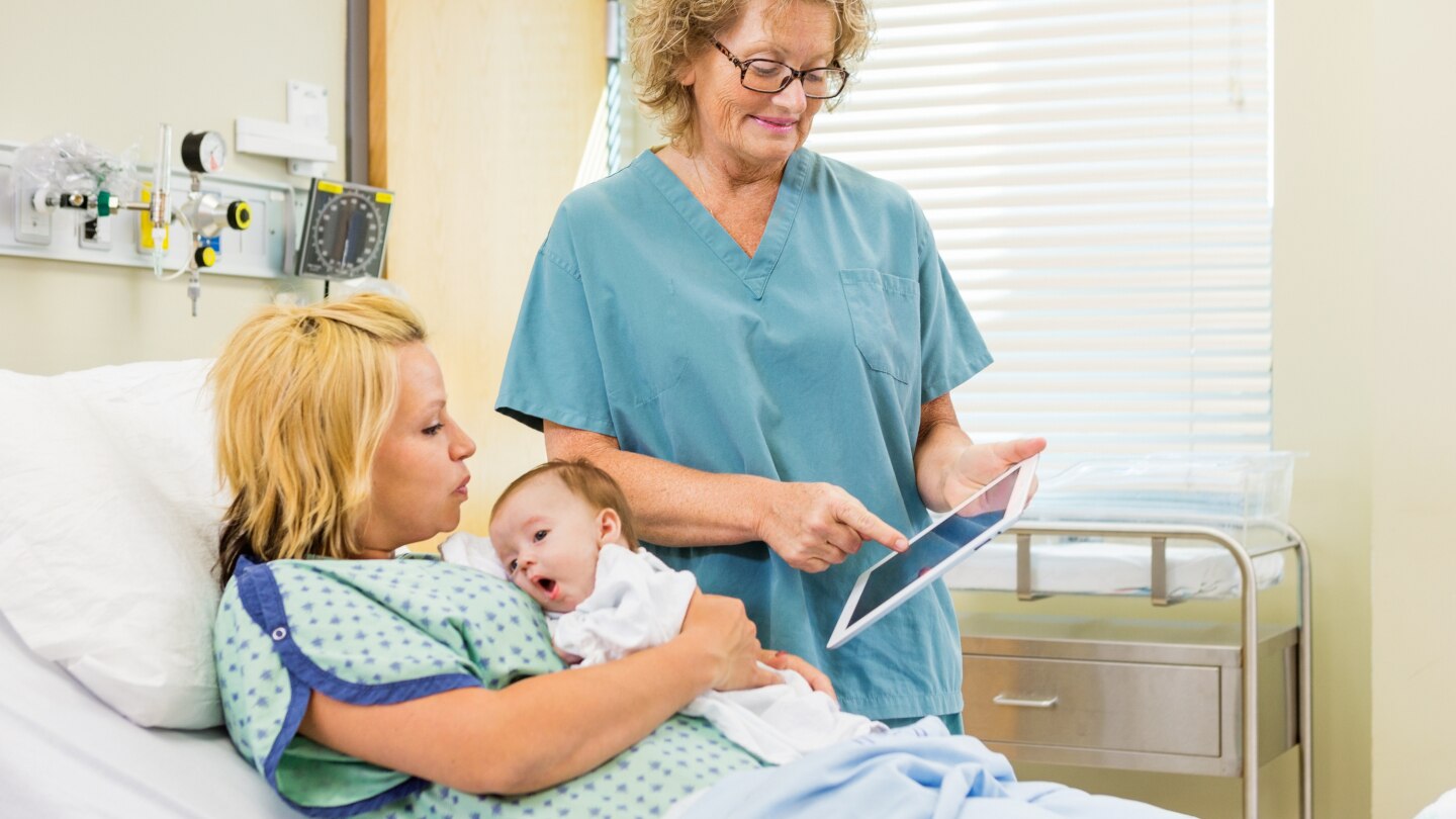 Nurse Explaining Reports On Digital Tablet To Woman With Babygir